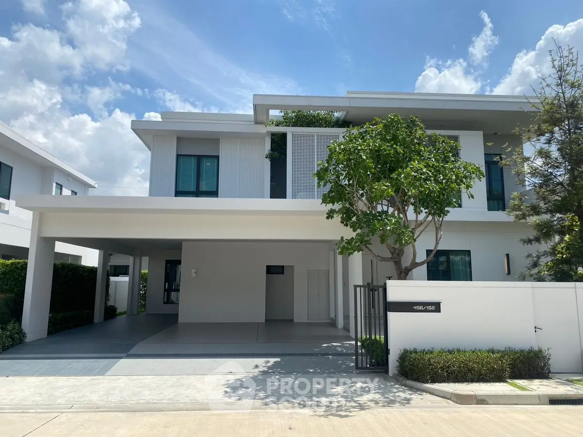 Modern two-story house with spacious driveway and lush greenery under a clear blue sky.