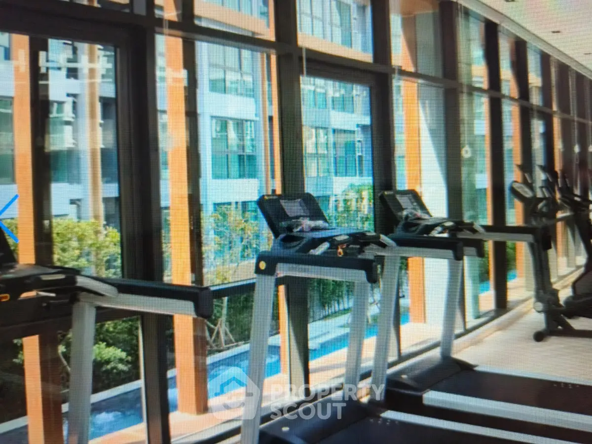 Modern gym with treadmills and large windows overlooking a pool and garden area.