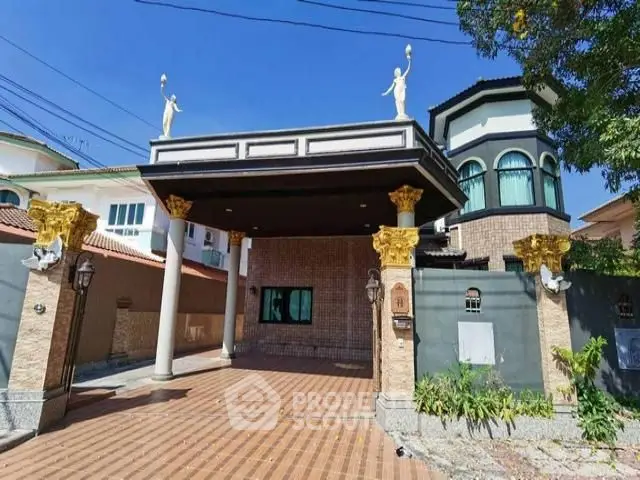 Luxurious entrance of a grand estate with elegant statues and spacious driveway.