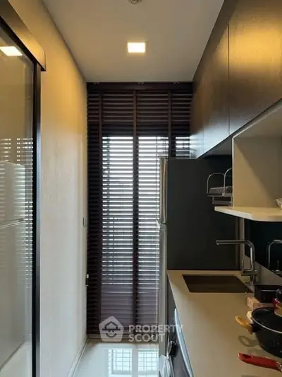 Modern kitchen with sleek cabinetry and natural light through window blinds.