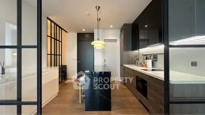 Modern kitchen with sleek black cabinetry and island, featuring elegant lighting and wood flooring.