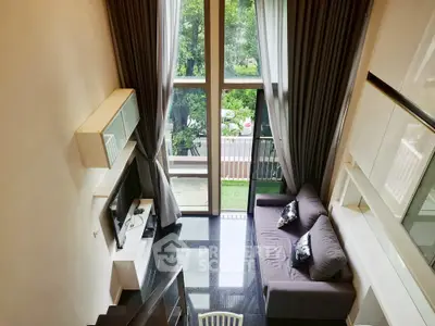 Spacious modern living room with high ceiling and large windows overlooking greenery.