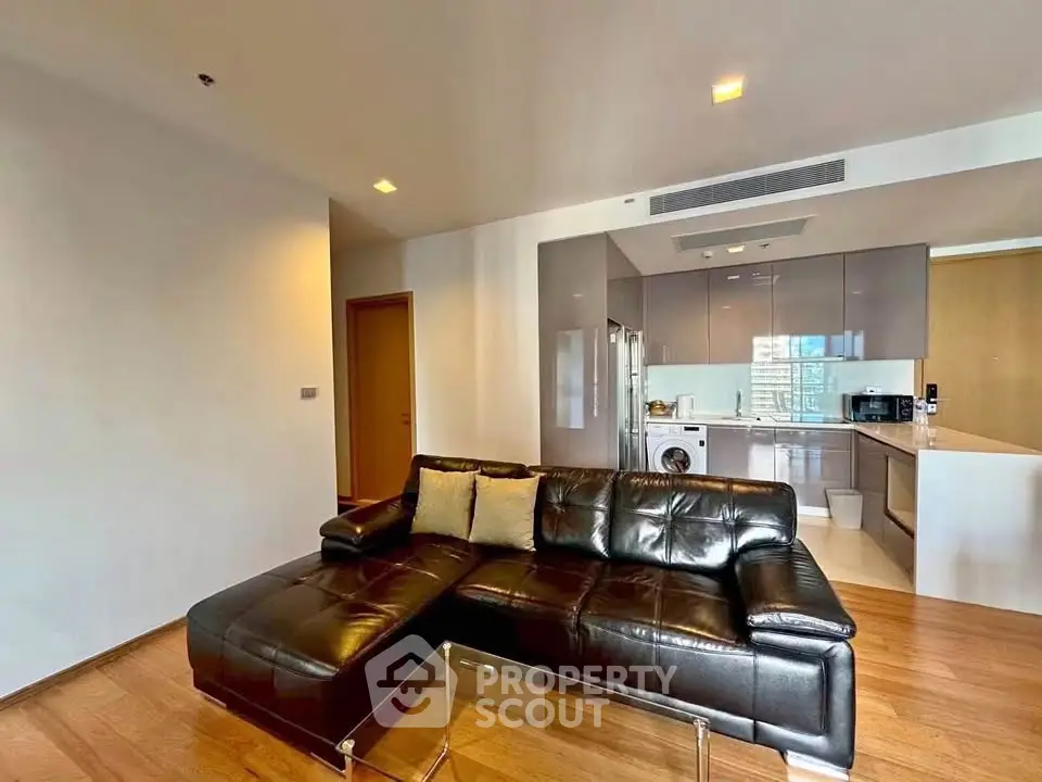 Modern open-layout living room with sleek leather sofa and integrated kitchen featuring stainless steel appliances.