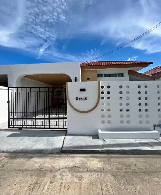 Modern white house exterior with unique circular design elements and gated entrance under a clear blue sky.