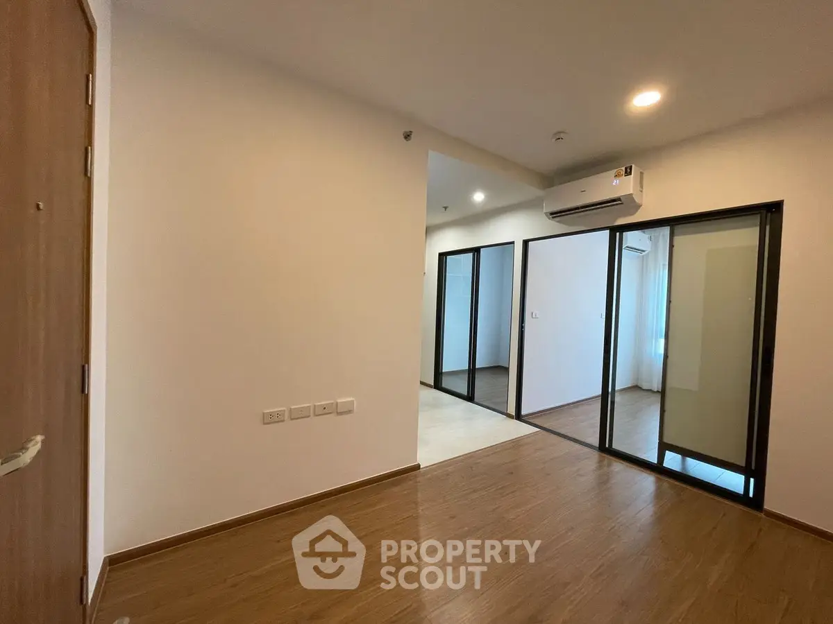 Modern apartment interior with wooden flooring and glass partition, featuring air conditioning.