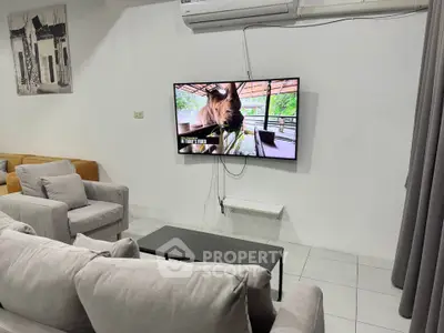Modern living room with cozy seating and wall-mounted TV under air conditioning unit.