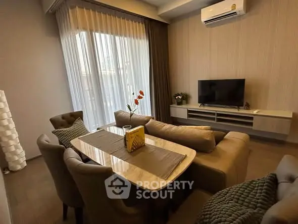 Elegant living room with modern furniture and natural light, featuring a cozy dining area and wall-mounted TV.