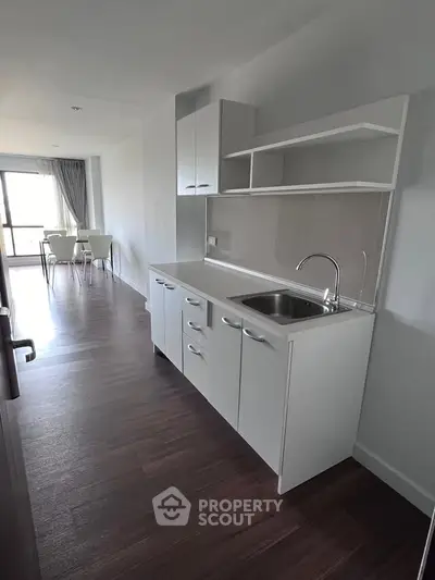 Modern kitchen with sleek cabinetry and open layout leading to dining area with natural light.
