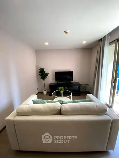 Modern living room with cozy sofa and TV, bright natural light from large window.