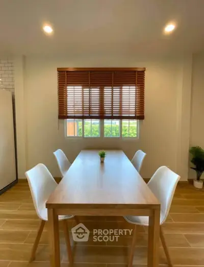 Modern dining area with wooden table and white chairs, featuring stylish blinds and natural light.