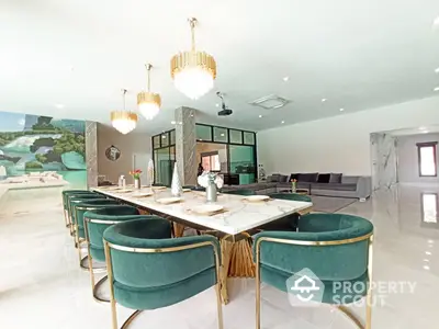 Luxurious open-plan living space with elegant green velvet chairs, a long dining table, and chic hanging lights, perfect for entertaining.