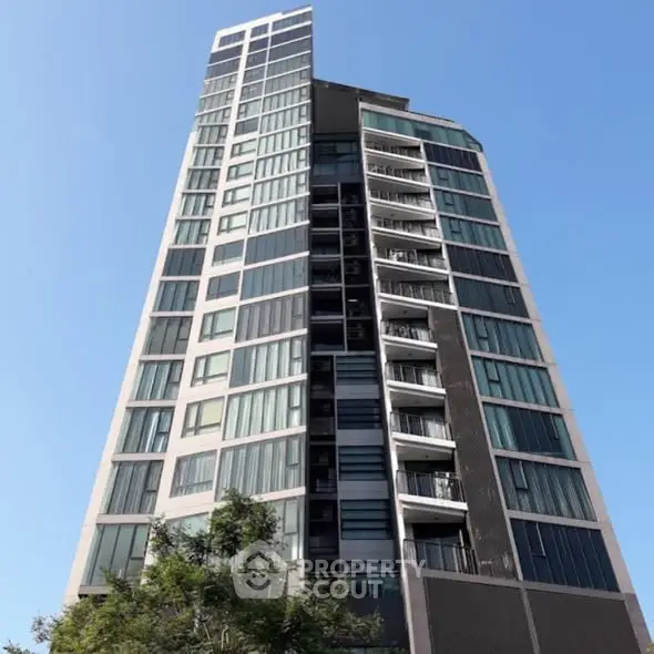Modern high-rise building with sleek glass facade and clear blue sky backdrop.