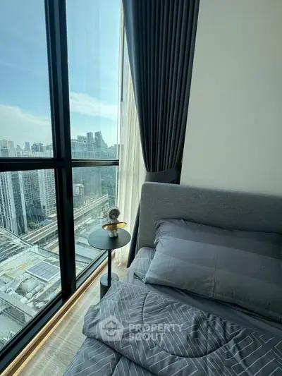 Modern bedroom with floor-to-ceiling windows offering stunning city views, featuring elegant decor and cozy bedding.