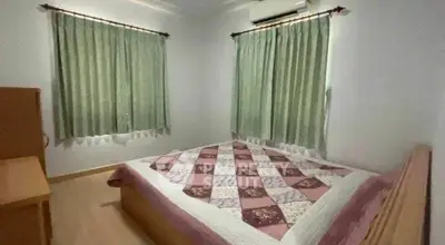 Cozy bedroom with quilted bedspread and natural light from two windows.