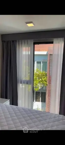 Modern bedroom with large window and elegant curtains offering a view of the building exterior.