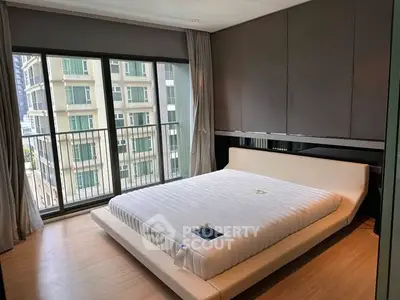 Modern bedroom with large windows and city view, featuring a minimalist bed and sleek design.