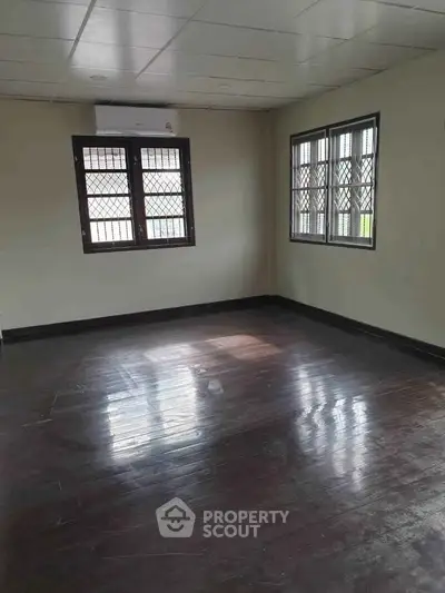 Spacious empty room with wooden flooring and large windows, perfect for customization.
