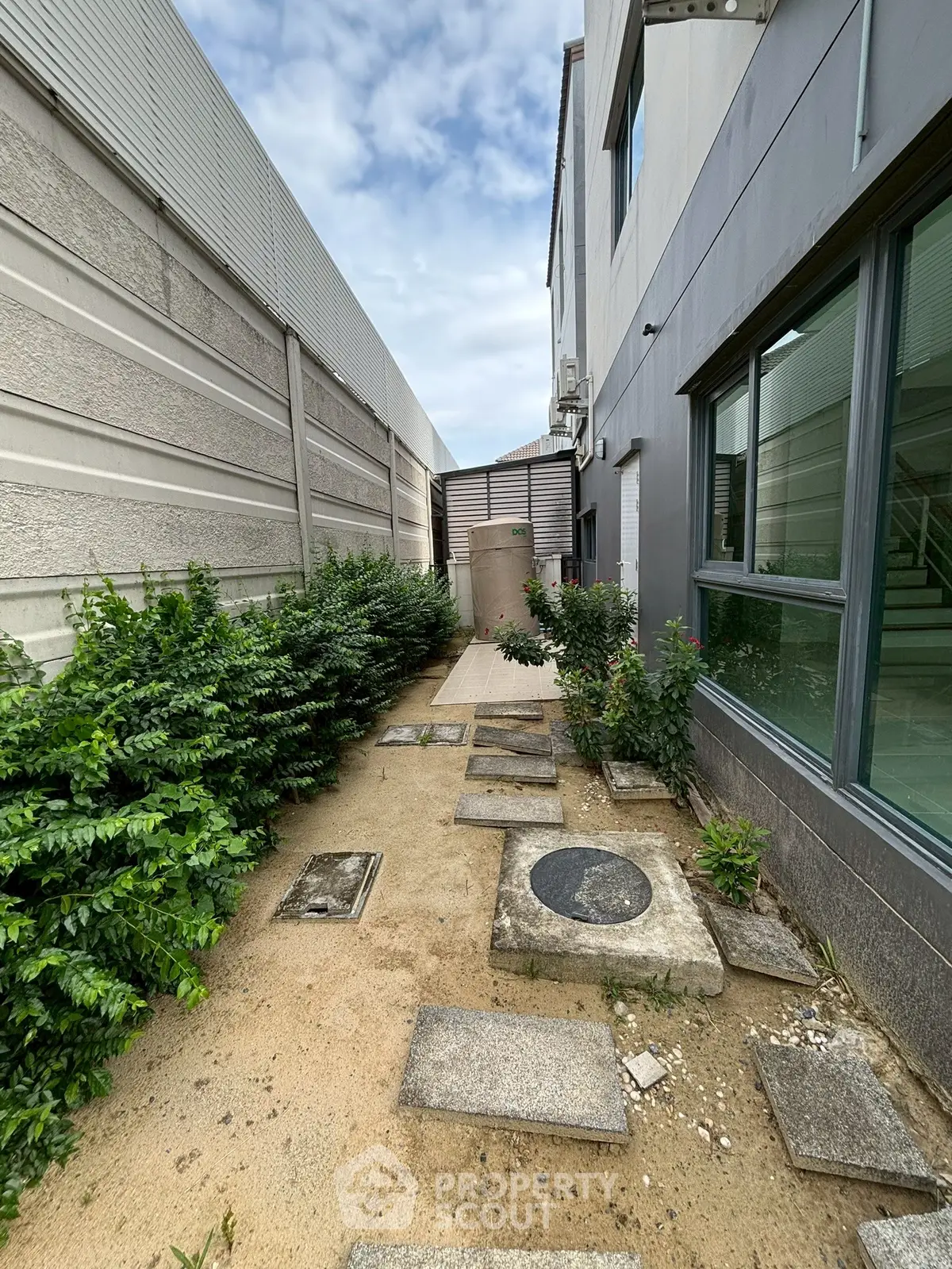 Narrow exterior pathway with stepping stones and greenery beside a modern building.