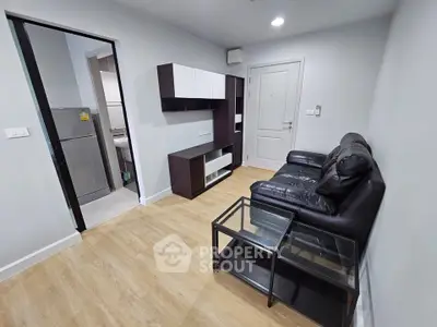 Modern living room with sleek black leather sofa and glass coffee table, adjacent to a compact kitchen area.