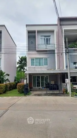 Modern three-story townhouse with a small garden and driveway in a suburban neighborhood.