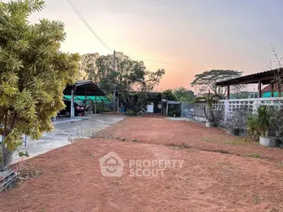 Spacious outdoor area with potential for landscaping at sunset, featuring a carport and mature trees.