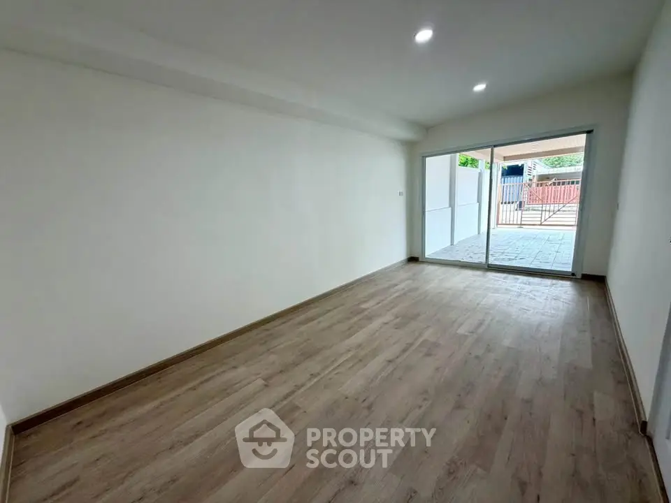 Spacious empty room with wooden flooring and large sliding glass doors leading to a patio.