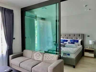 Modern apartment with glass partition separating living room and bedroom, featuring stylish furniture.