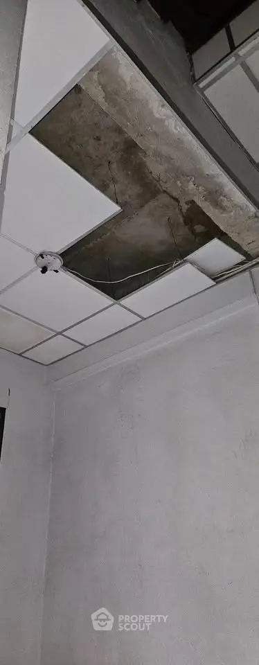 Ceiling with missing tiles revealing structural elements in a room.