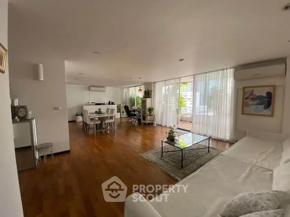 Spacious living room with wooden floors, large windows, and elegant decor in a modern apartment.