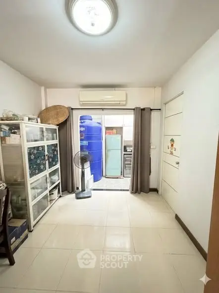 Spacious room with storage cabinets and air conditioning, leading to a utility area with large water tank.