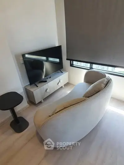 Modern living room with stylish curved sofa and flat-screen TV, featuring sleek wooden flooring and natural light.