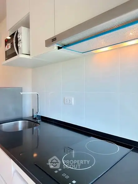 Modern kitchen with sleek induction cooktop and built-in microwave, featuring minimalist design and glossy finishes.