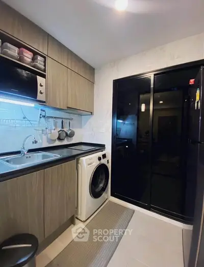 Modern kitchen with sleek cabinetry, washing machine, and microwave in a compact layout.