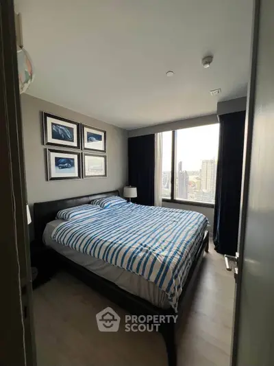 Modern bedroom with large window and city view, featuring stylish decor and comfortable bedding.