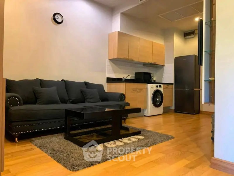 Modern living room with open kitchen, featuring sleek furniture and wooden flooring.