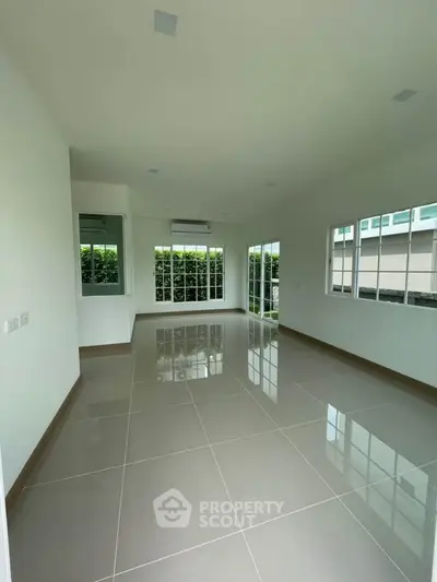 Spacious modern living room with large windows and glossy tiled floors, offering abundant natural light.