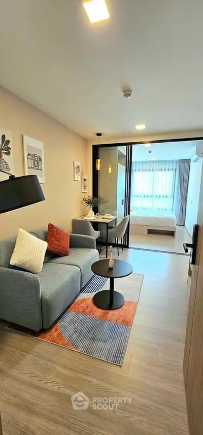 Modern open-plan living room with cozy seating and stylish decor leading to a bright bedroom.