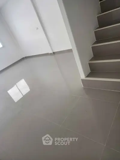 Spacious modern interior with sleek tiled flooring and staircase, ideal for customization.