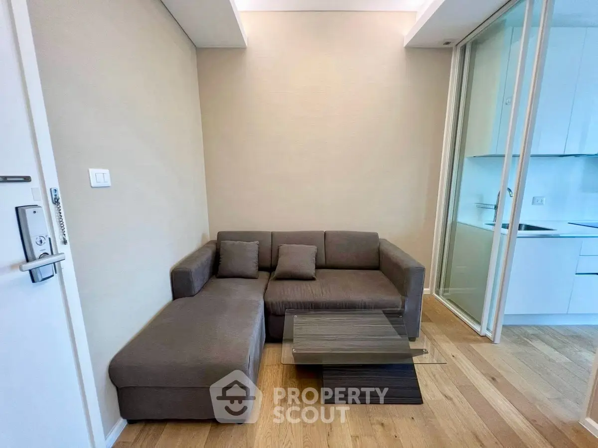 Modern living room with sleek sofa and wooden flooring adjacent to a compact kitchen.