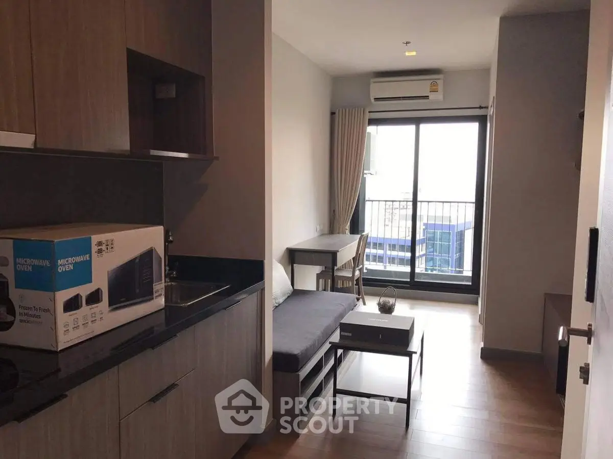 Modern studio apartment with kitchenette and balcony view, featuring sleek wooden flooring and contemporary furnishings.