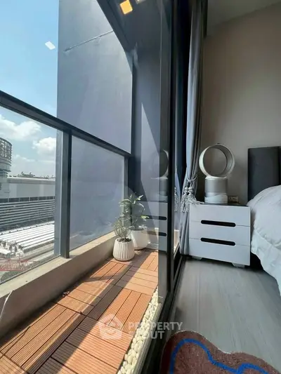 Modern bedroom with floor-to-ceiling windows and small balcony offering city views.