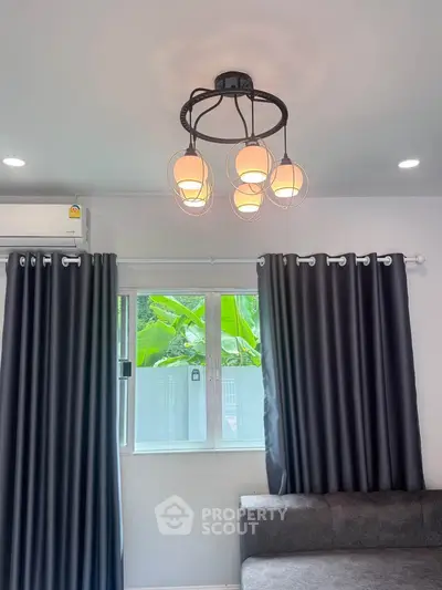 Modern living room with stylish lighting and large window, featuring elegant curtains and a cozy sofa.