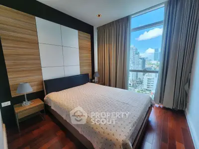Modern bedroom with large window offering city view, featuring wooden flooring and stylish decor.