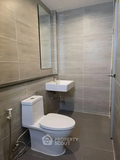 Modern bathroom with sleek design and neutral tiles, featuring a wall-mounted sink and toilet.