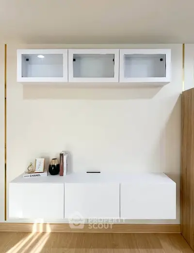 Modern minimalist living room with sleek white cabinets and wooden flooring.