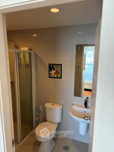 Modern bathroom with shower, toilet, and sink in a sleek apartment setting.