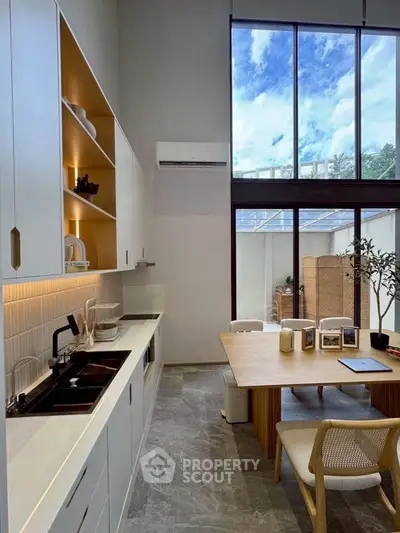 Modern kitchen with high ceilings and large windows, featuring sleek cabinetry and a stylish dining area.