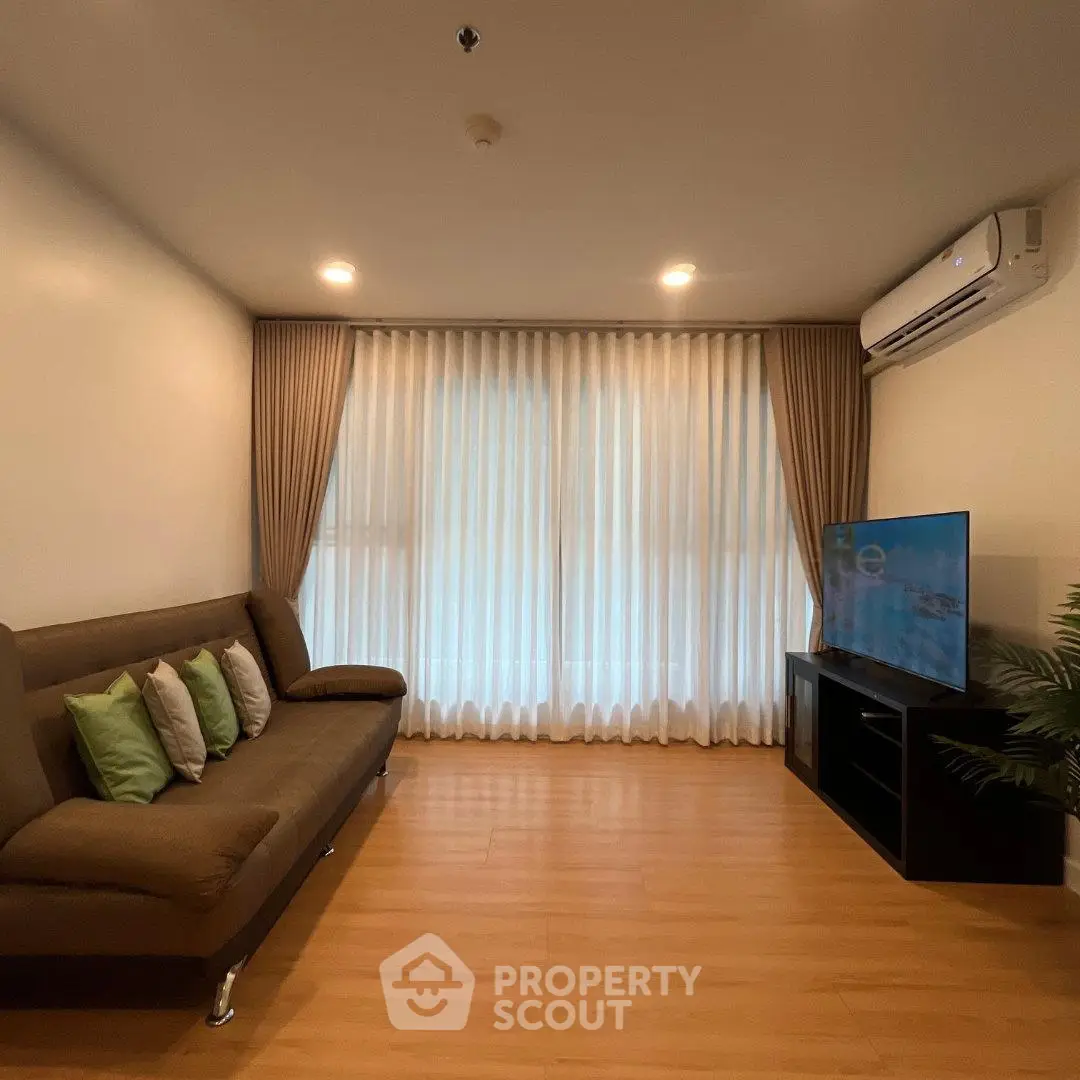 Modern living room with sleek sofa, TV, and air conditioning, featuring elegant curtains and wooden flooring.