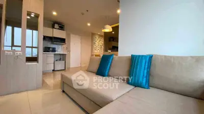 Modern living room with beige sofa and blue cushions, open kitchen layout, and stylish decor.