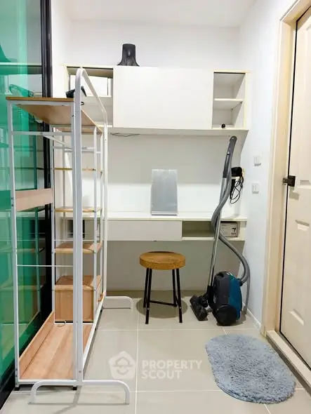 Compact study area with desk, shelves, and vacuum cleaner in modern apartment.